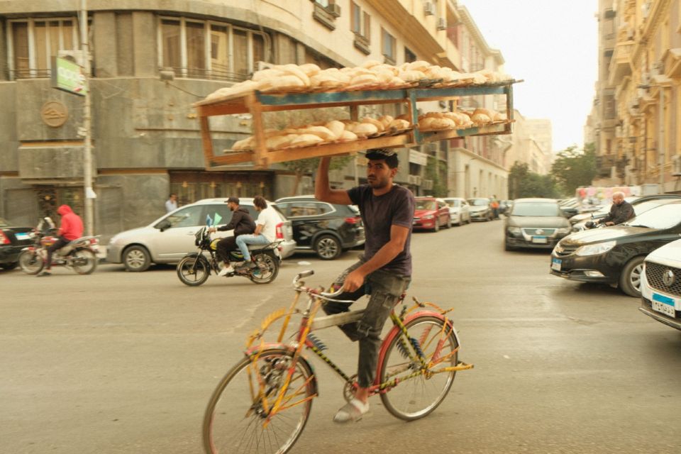 A bread seller cycles through busy Cairo traffic balancing a wooden tray of loaves on his head.