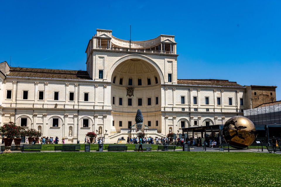 The Vatican Museums exterior and courtyard in Vatican City, with visitors gathered outside under a clear sky.