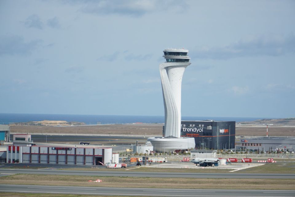 Istanbul Airport का कंट्रोल टॉवर साफ आसमान के नीचे रनवे और टर्मिनल इमारतों के ऊपर दिखाई देता है.