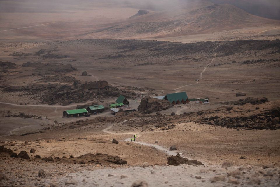 Escursionisti si avvicinano a un gruppo di rifugi dal tetto verde sul percorso Marangu del Kilimangiaro.