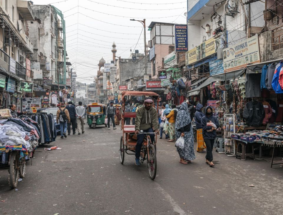 Un conducente di risciò a pedali attraversa una trafficata via del mercato nella Old Delhi, Delhi.