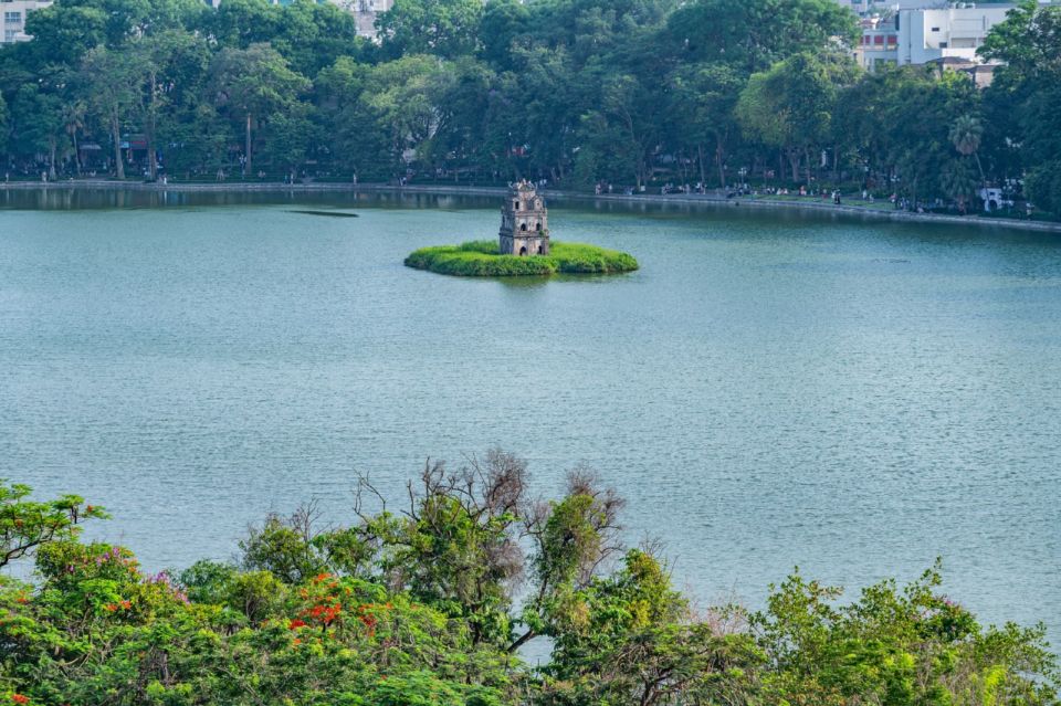Turtle Tower sits on a small island in Hoan Kiem Lake, Hanoi, surrounded by green trees.