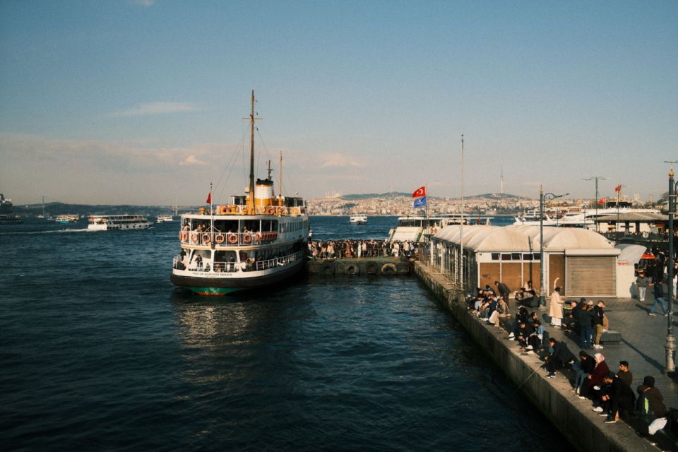 En passagerfærge lagt til kaj ved en travl mole i Istanbul med byens skyline på den anden side af vandet.
