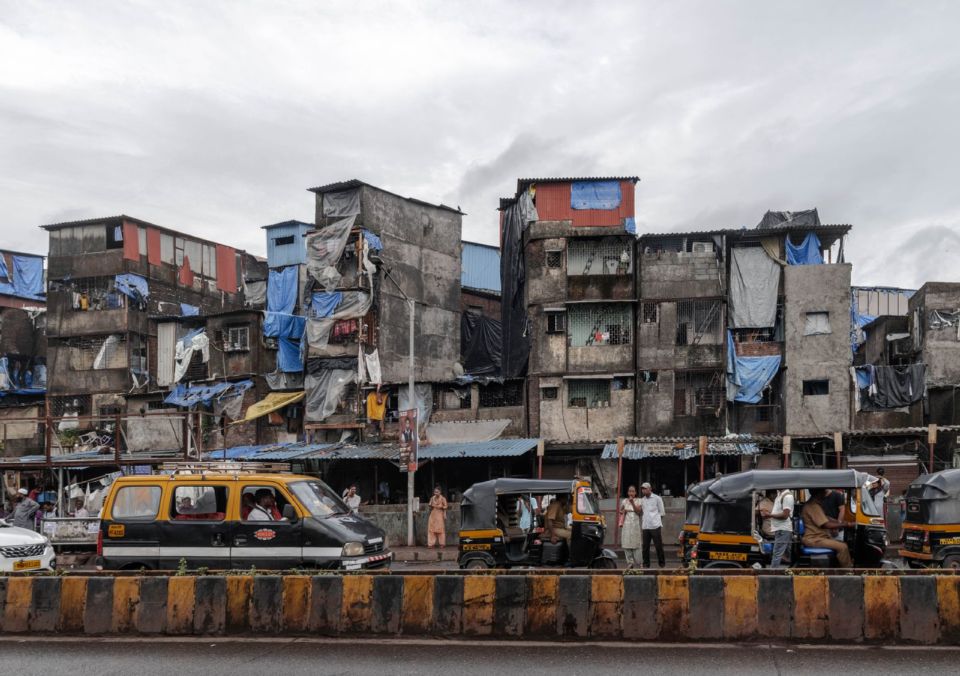 Mumbajas iela ar cieši izvietotām mājām un auto rikšām, kas raksturīga Dharavi rajonam.