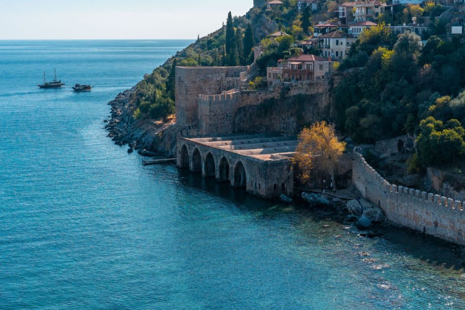 Alanya's clifftop castle walls and old shipyard arches rise above the sea, with boats passing below.