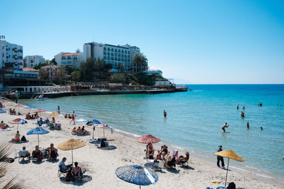 Ufukwe wa mchanga wenye miavuli na waogeleaji kando ya maji safi ya Kuşadası