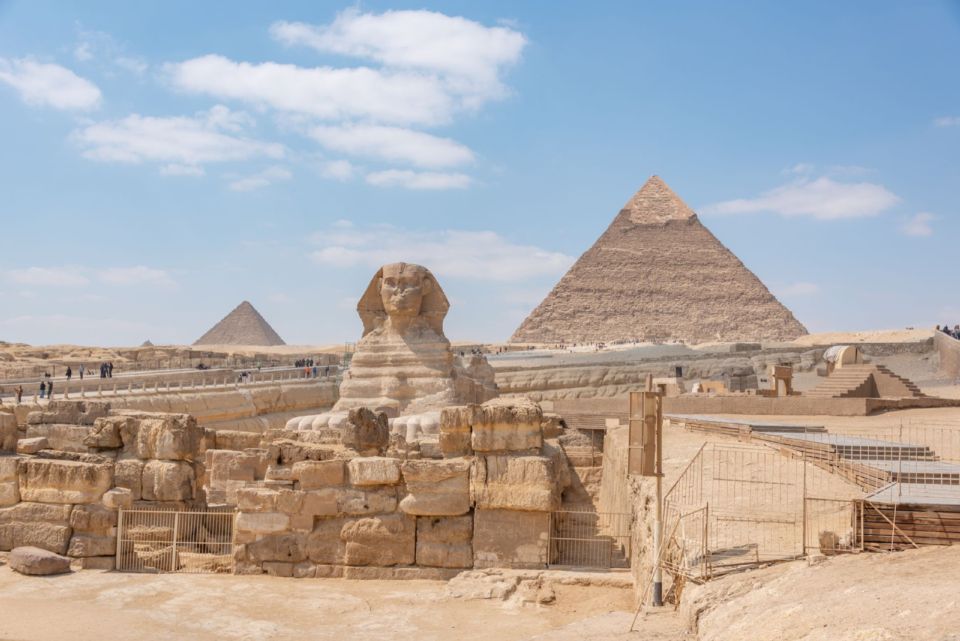 The Great Sphinx of Giza with the pyramids behind it under a blue sky in Cairo, Egypt.