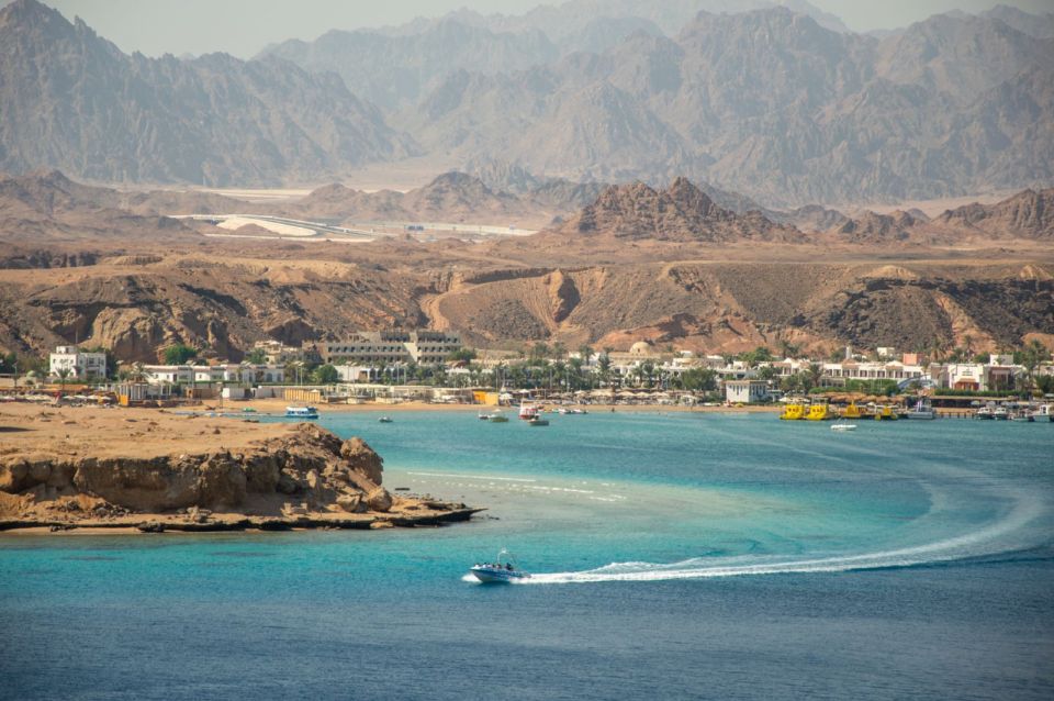 A coastal view of Sharm El Sheikh with a motorboat on the sea and desert mountains behind.