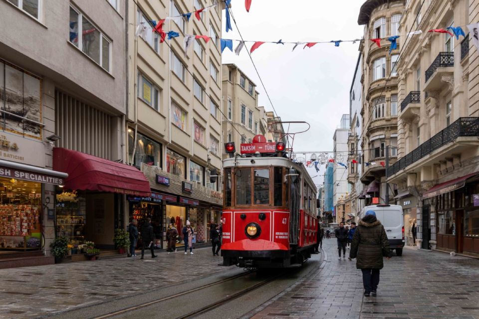 A red heritage tram runs along Istiklal Avenue in Istanbul on a daytime street lined with shops.