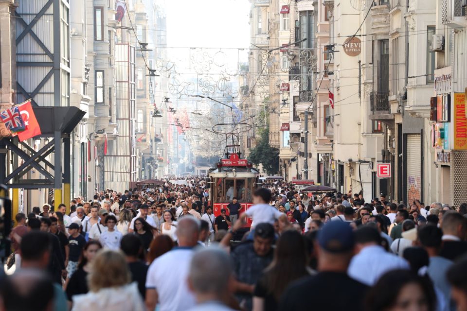 Istiklal Avenue in Istanbul filled with pedestrians and a historic tram running through the crowd in daylight.