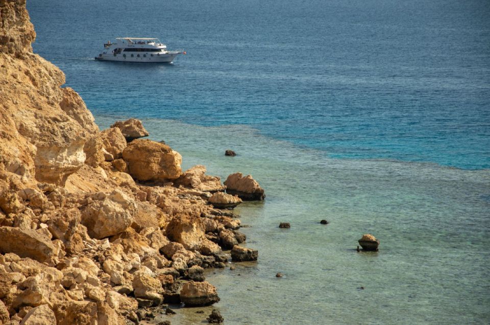 Rocky cliffs and clear sea at Ras Mohammed National Park with a tour boat offshore.