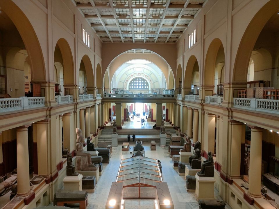 Main hall of the Egyptian Museum in Cairo, lined with ancient statues and arched upper gallery.
