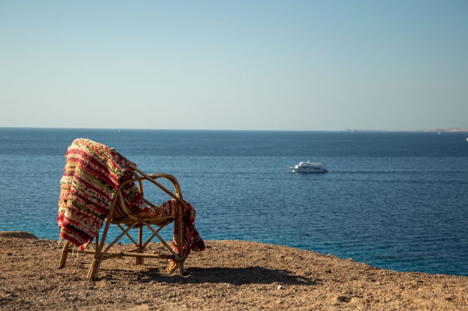 A seafront chair overlooks the calm blue waters of the Red Sea near Hurghada, with a boat passing by.