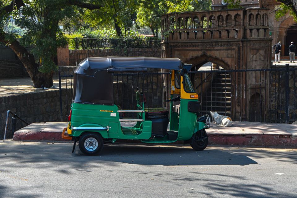 A green auto rickshaw parked on a Delhi street beside a historic sandstone building.